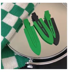 Detail of matte green and black no-crease hair clips with logo on a reflective mirror
