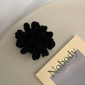 Close-up of black plush scrunchie with fluffy chenille texture on a minimal background