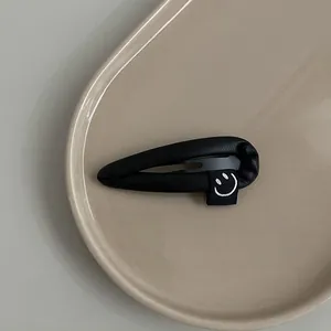 Detailed close-up of a black PU leather droplet hair clip with a cute smiley face tag