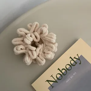 Close-up of a plush cream chenille hair scrunchie on a minimalist green background