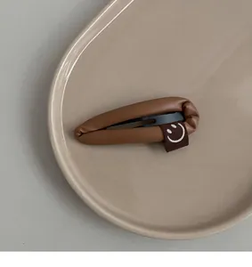 Detail of a brown leather hair clip with a cute smiley face tag on a ceramic tray