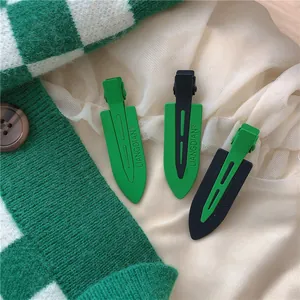 Set of matte green and black duckbill hair clips with embossed lettering on knit fabric