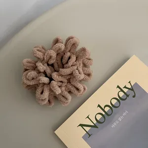 Close-up of soft light brown plush hair scrunchie on a minimalist grey desk setup