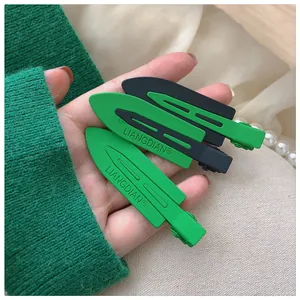 Detail of matte green and black metal hair clips featuring letter engraving on a beige fabric