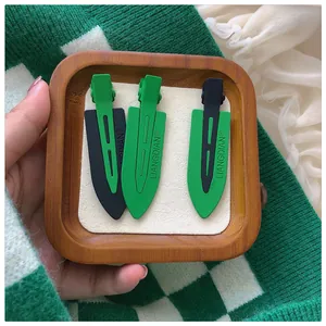 Detailed view of three green and black matte duckbill hair clips in a wooden tray
