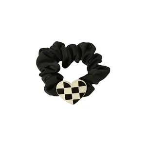 Chic black satin scrunchie with a checkerboard heart charm for women's hair styling