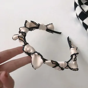 Close-up of cream satin headband with black lace trim and retro ruffled wave design
