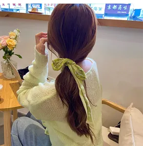 Detail of light green floral chiffon hair ribbon tied as a bow on a ponytail hairstyle