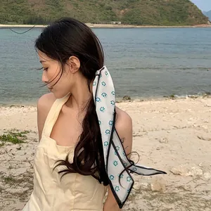 Detail of white chiffon hair scarf with blue smiley patterns tied in a long ponytail