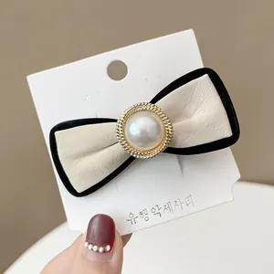 Detail of a beige leather bow hair clip with central pearl and golden wheat trim