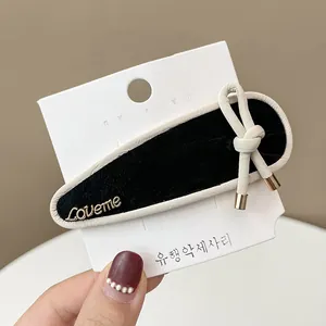 Detail of velvet water drop hair clip with gold Loveme lettering and cream bow accent