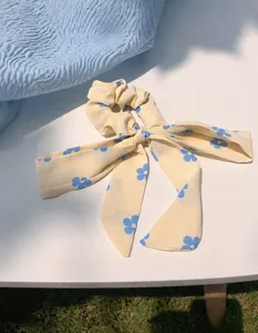 Detail eines cremefarbenen Blumen-Haargummis mit langer Schleife und blauem Muster