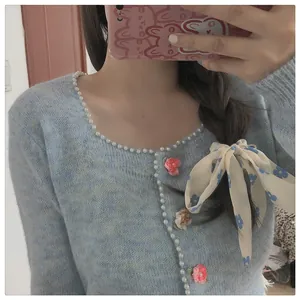 Detail der hellblauen flauschigen Strickjacke mit Perlenbesatz und rosa Blumen-Verzierung