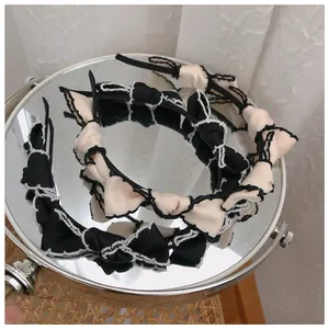 Detail of ruffled lace headbands in black and beige displayed on a reflective mirror