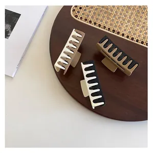 Three minimalist matte rectangular hair claws in mixed earth tones on a wooden tray