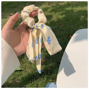 Detailaufnahme von cremefarbenem Blumen-Haargummi mit blauem Muster und Schleife