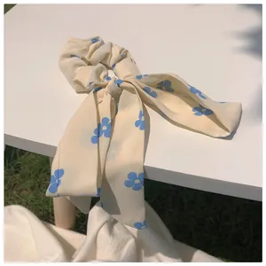 Detail eines cremefarbenen Blumen-Haargummis mit langen Bändern auf einer Parkbank