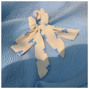 Detail eines cremefarbenen Haargummis mit blauem Kleeblatt-Blumendruck und Bändern