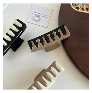 Three rectangular matte bicolor hair claws in black, white, and brown on a wooden tray