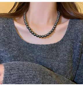 Dettaglio di una collana di perle grigio scuro su modella con maglia grigia