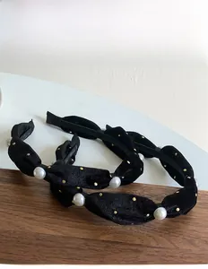 Detail of velvet headbands featuring white pearls and gold accents on a knotted black texture