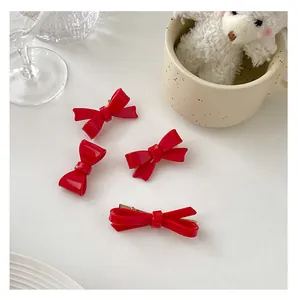 Close-up of four red bow hair clips on a clean white table with decorative elements