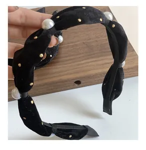 Detailed view of black velvet headband with white pearls and gold metal rivets texture