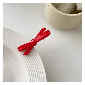 Detail of a glossy red resin bow hair clip clipped on a white ceramic plate