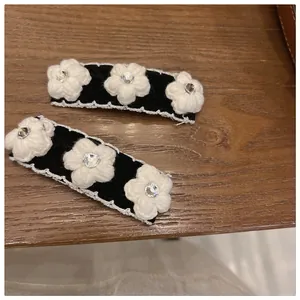 Detail of camellia knit hair clips with white yarn flowers and rhinestones on black fabric