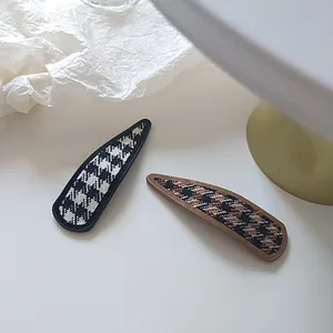Macro detail of houndstooth fabric texture on teardrop-shaped metal BB hair clips