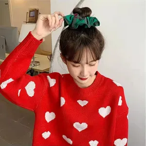 Close-up of a festive green plaid hair scrunchie worn by a model in a red heart sweater