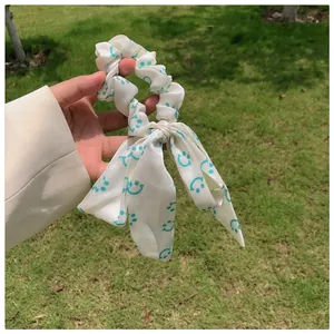 Détail du chouchou crème avec longs rubans et motifs de smileys verts sur le tissu