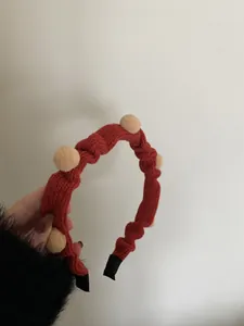 Detail eines roten gestrickten Weihnachts-Haarreifens mit beige Pompons und Faltenstoff
