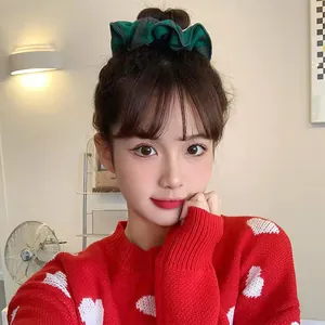 Close-up of a green and black plaid scrunchie worn by a model in a cozy setting