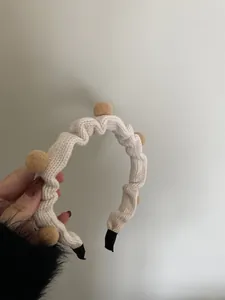 Detailansicht beige gestricktes Stirnband mit braunen Bommeln und gerippter Textur