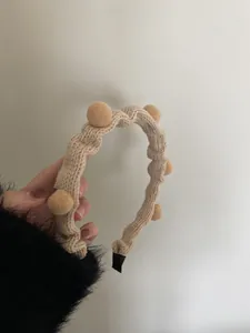 Detail eines beigen Strickstirnbandes mit Bommeln, Rippenstruktur und weichen Enden