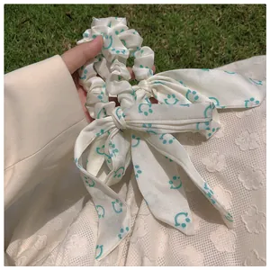 Détail du motif smiley bleu sarcelle sur le chouchou à ruban en soie de couleur crème