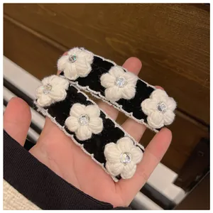 Detail of two black velvet hair clips featuring white knit flowers and tiny diamonds