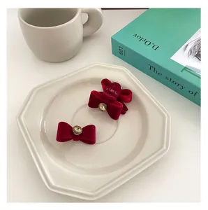 Detail of burgundy velvet bow hair clips with central rhinestone on a ceramic plate