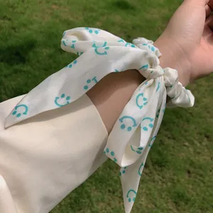 Chouchou à ruban couleur crème avec motif smiley bleu sur fond d'herbe naturelle