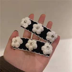 Handheld view of two black velvet hair clips with white knitted camellias and small rhinestones