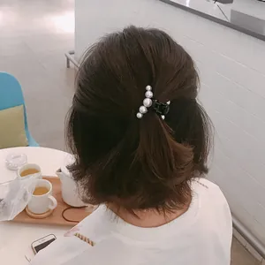 Elegant medium hair claw clip with white pearls worn on dark brown hair in a cafe setting