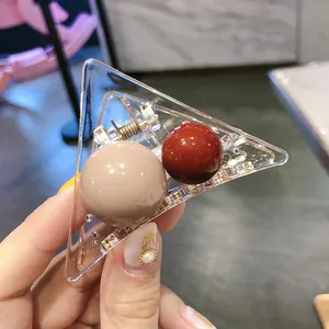 Detail of transparent triangle shark hair clip with beige and dark red spherical beads
