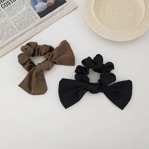 Close-up of black and brown satin bow scrunchies with elegant textured fabric on cream background