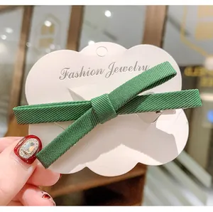 Detail of a dark green ribbon bow hair clip on a white cloud-shaped display card