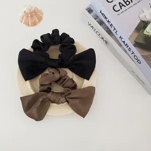Close-up of satin bow scrunchies in black and brown showing soft texture and pleated details