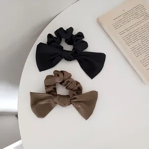 Detail of black and brown satin bow scrunchies displayed on a minimalist background