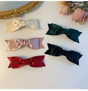 Detail of five satin bow hair clips in cream, pink, red, green, and black silk finish