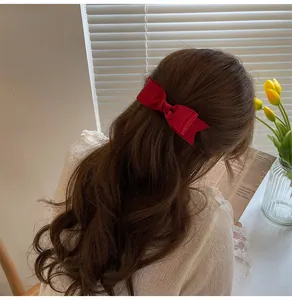 Close-up of deep red satin bow hair clip on a model with long wavy brown hair
