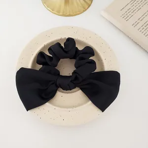 Detail of a black satin scrunchie with a large bow on a ceramic tray for elegant styling